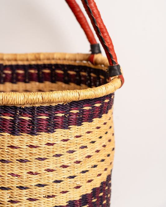 Close-up of medium Bolga laundry basket weave in burgundy and tan stripe with leather handle detail - handwoven elephant grass basket, Ghana