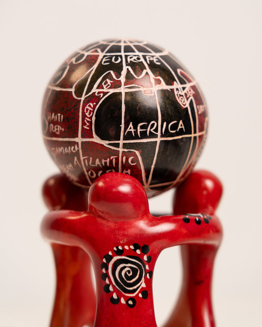 Close-up of the soapstone globe showing Africa and Europe above red figures with cream and black spiral decoration.