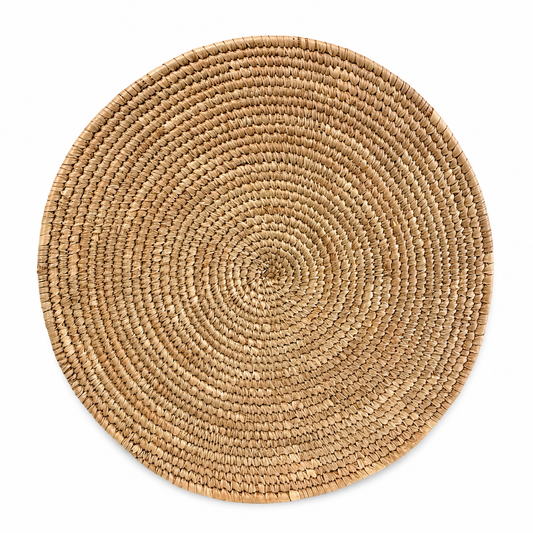 Handwoven natural seagrass round placemat on a white background featuring a circular woven design in natural beige tones.