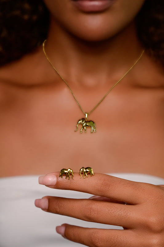 Woman wearing the Big 5 gold-plated elephant pendant necklace, holding the matching gold elephant stud earrings on her fingertip.
