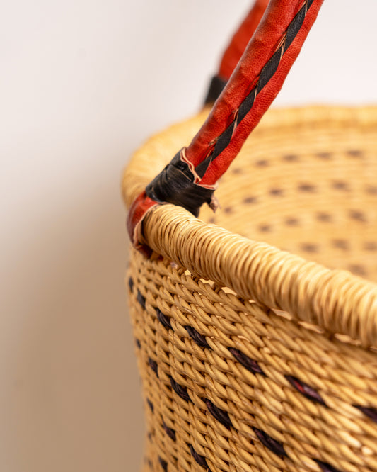 Close-up of the two-tone leather-wrapped handle on a brown and tan Bolga laundry basket, braided leather on handwoven elephant grass, Ghana