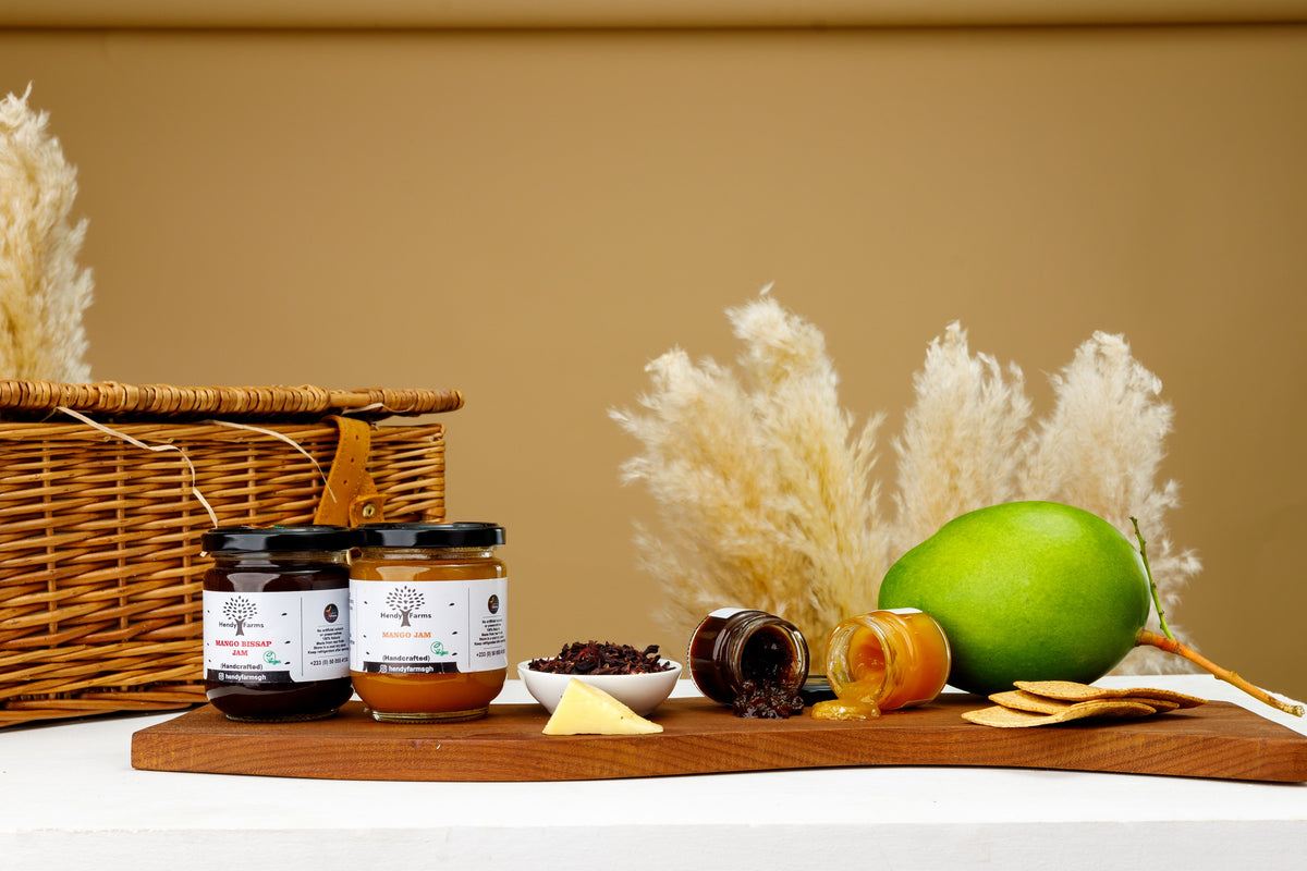 Hendy Farms mango jam and mango bissap jam on a wooden serving board with crackers, cheese and a fresh mango