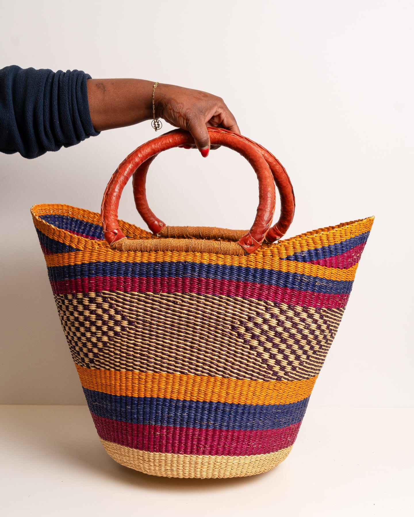 Colourful woven basket with red handles held by a person against a white background