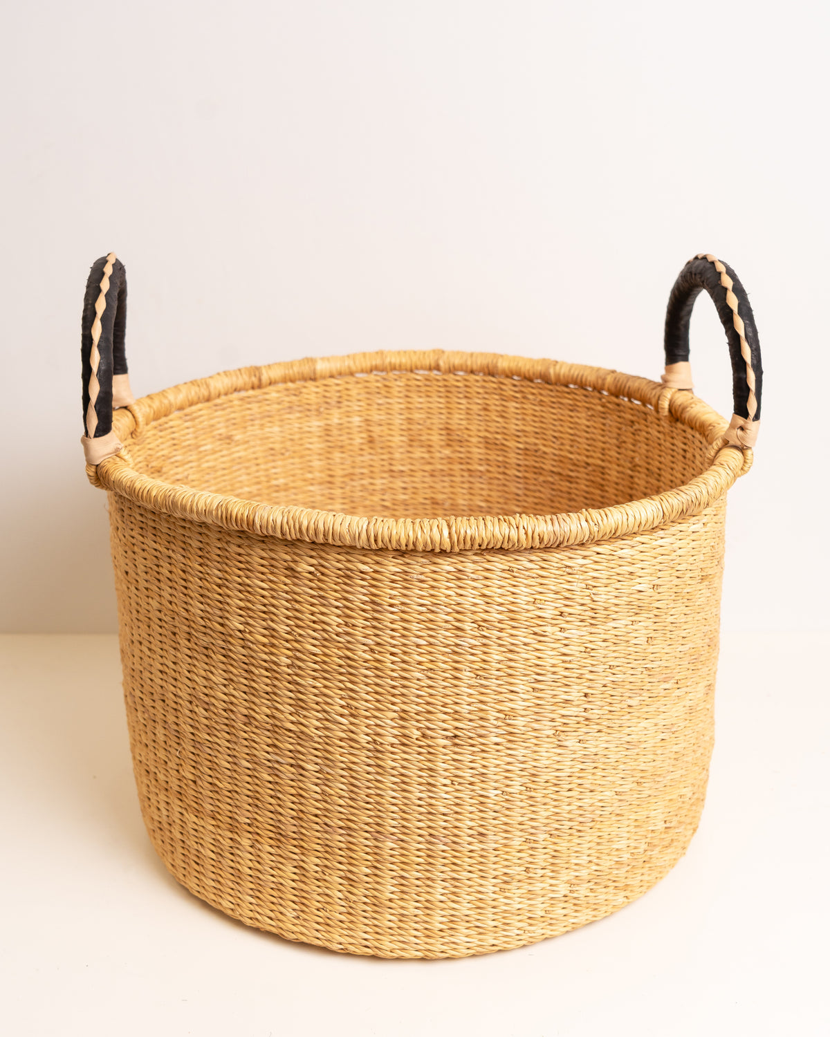 Front view of a large natural Bolga storage basket handwoven from elephant grass with contrasting black braided leather handles — Nathez Out of Africa

