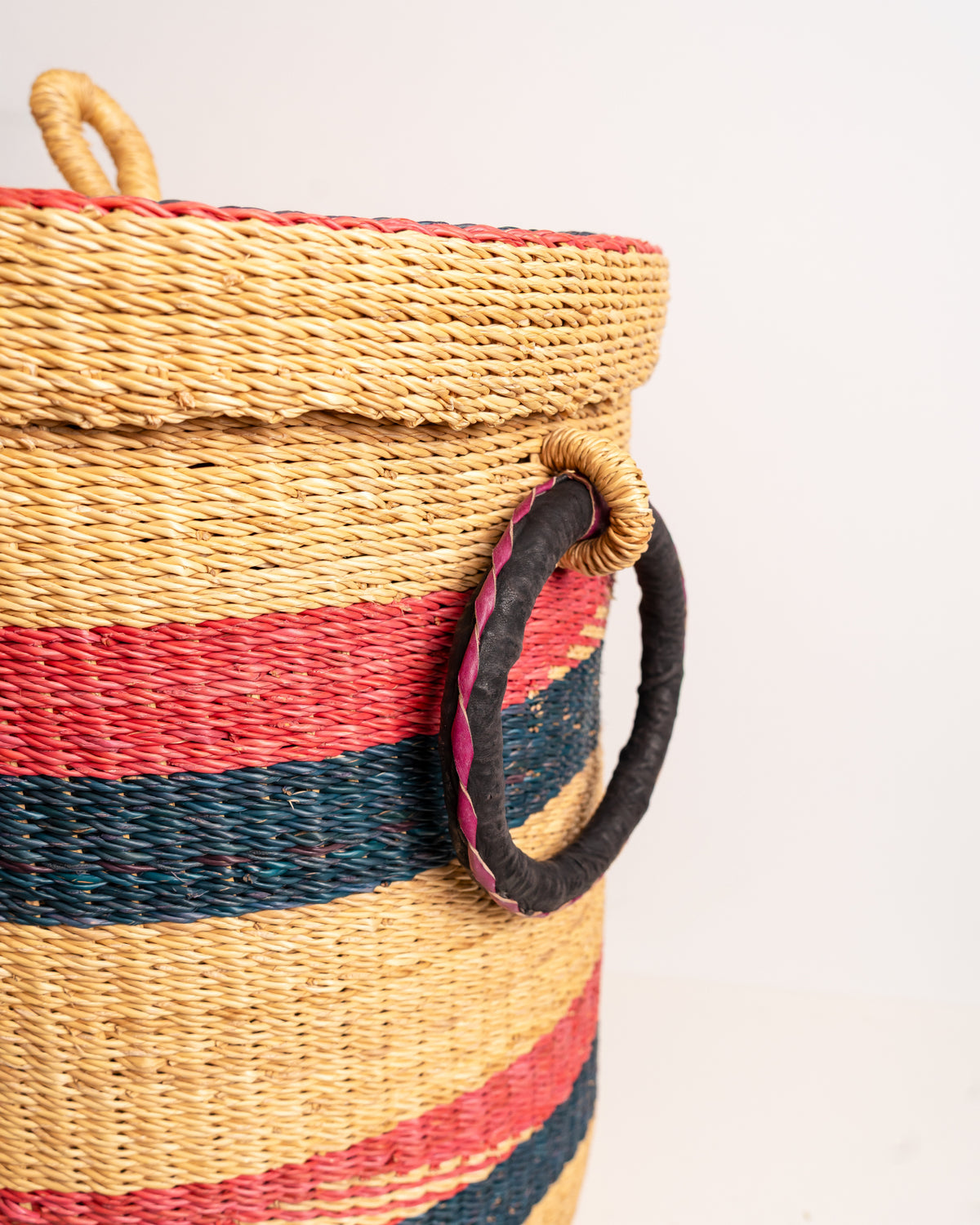 Close-up of leather-wrapped handle on handwoven Bolga laundry basket - red and navy striped elephant grass hamper, Ghana