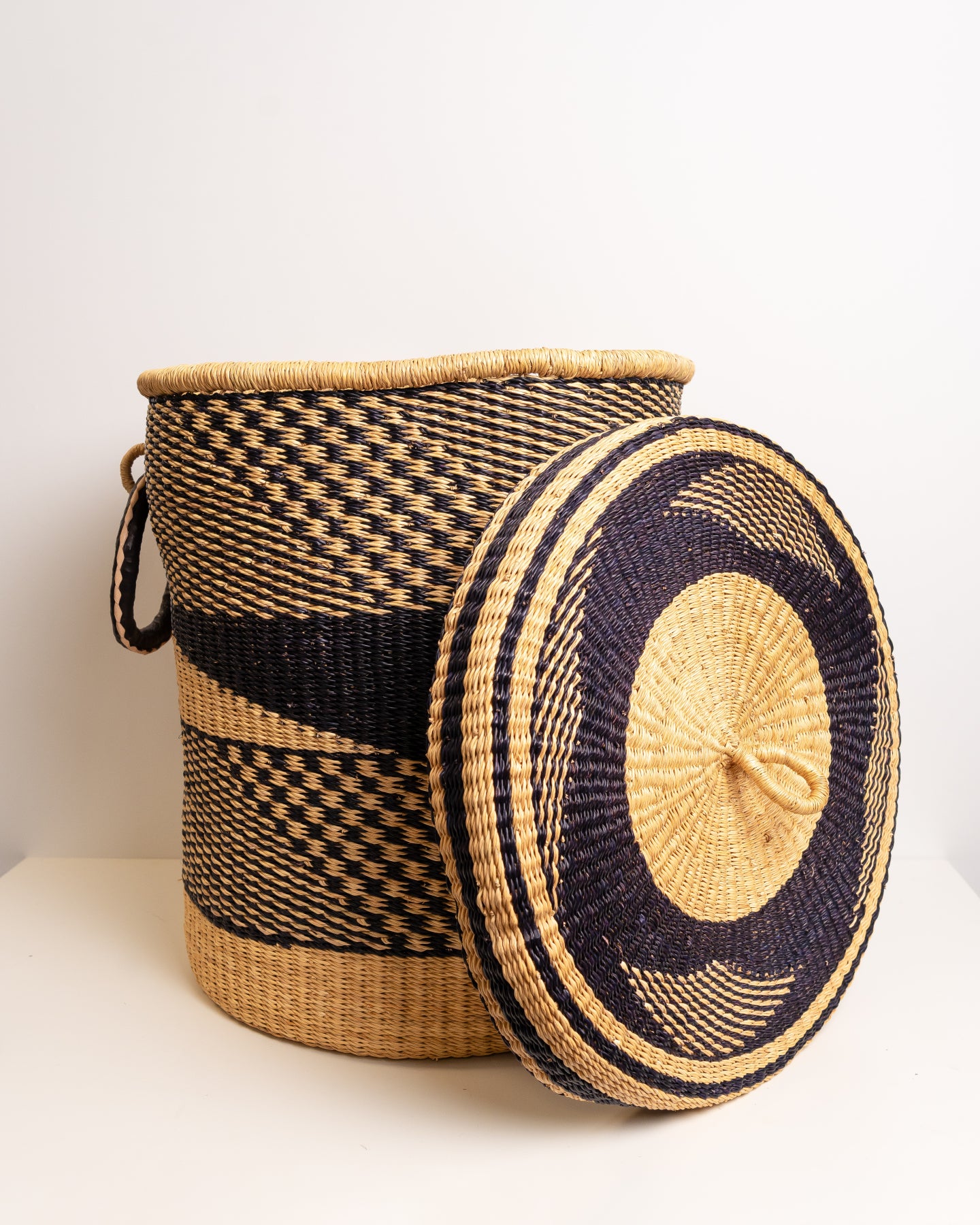 Handwoven Bolga laundry basket with round lid resting beside it, black and tan African storage basket, Ghana