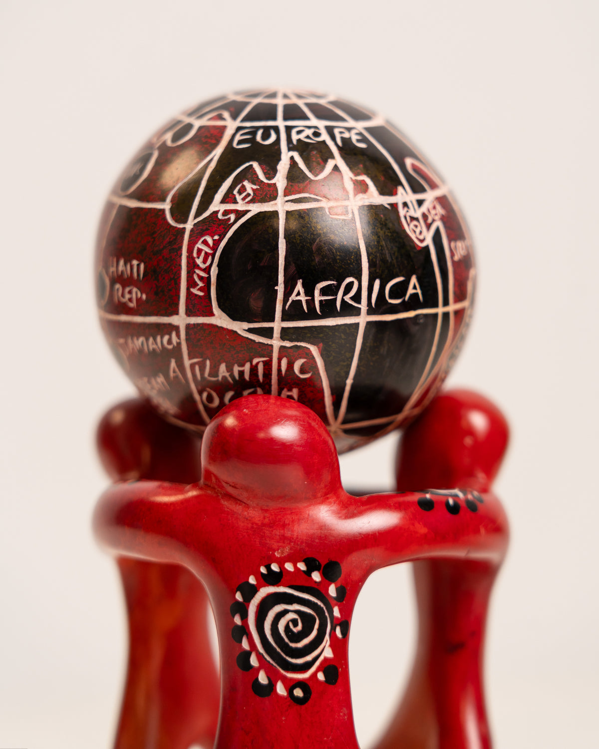 Close-up of the soapstone globe showing Africa and Europe above red figures with cream and black spiral decoration.
