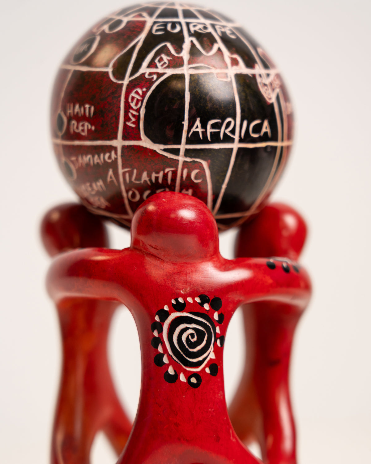 Detail of a red soapstone figure with a spiral motif beneath a globe with cream map outlines.