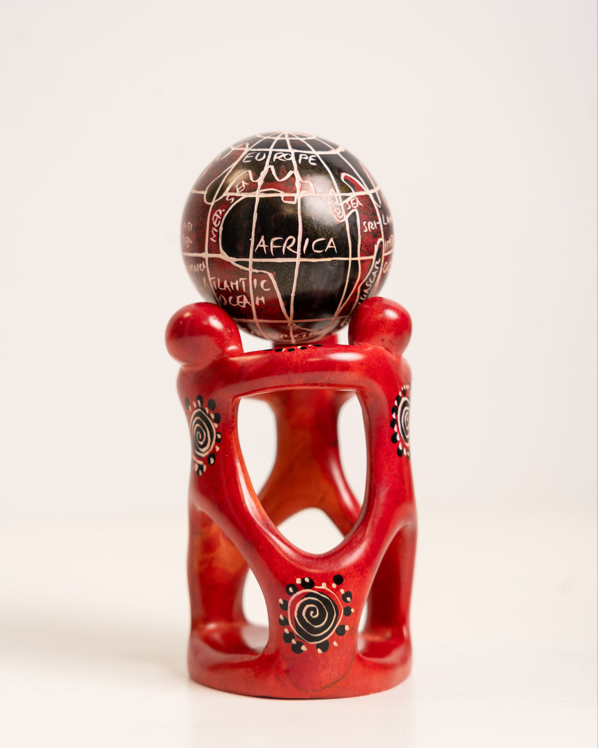 Angled view of the soapstone globe sculpture showing linked red figures, open carved spaces and a circular base.