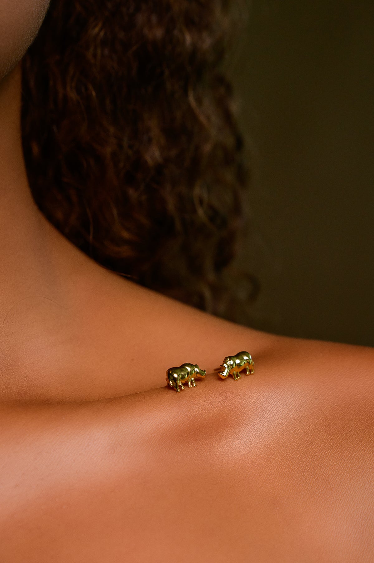 Pair of 18k gold-plated rhino stud earrings resting on a woman's shoulder - Big 5 rhino necklace and earring set by H2Wild