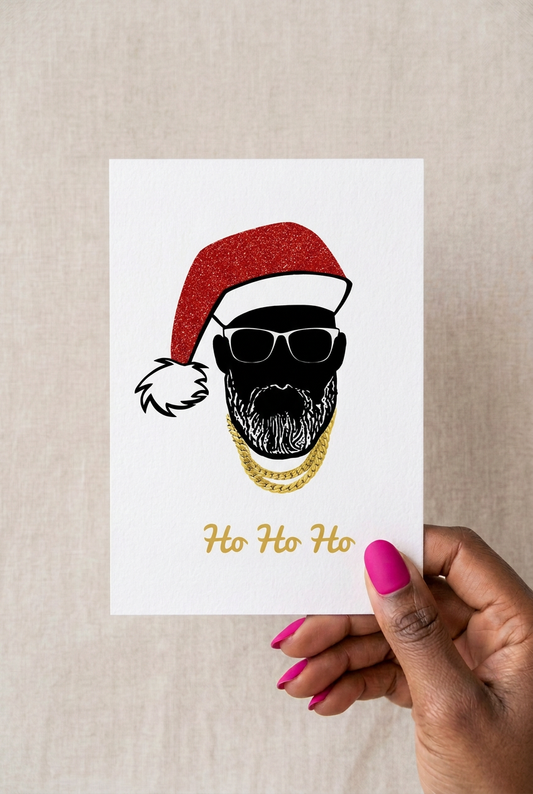 Hand holding a Black Santa Christmas card featuring sunglasses, a red Santa hat, gold chains and ‘Ho Ho Ho’ lettering.