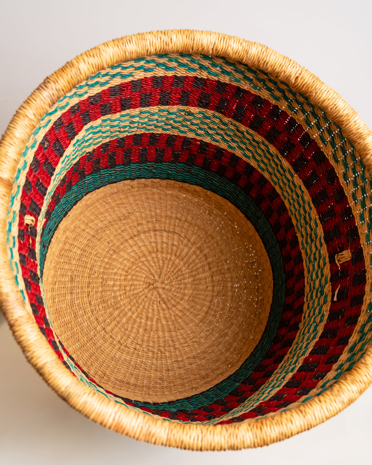 Top-down view into empty Bolga laundry basket, red, teal and black stripe, handwoven elephant grass, Ghana