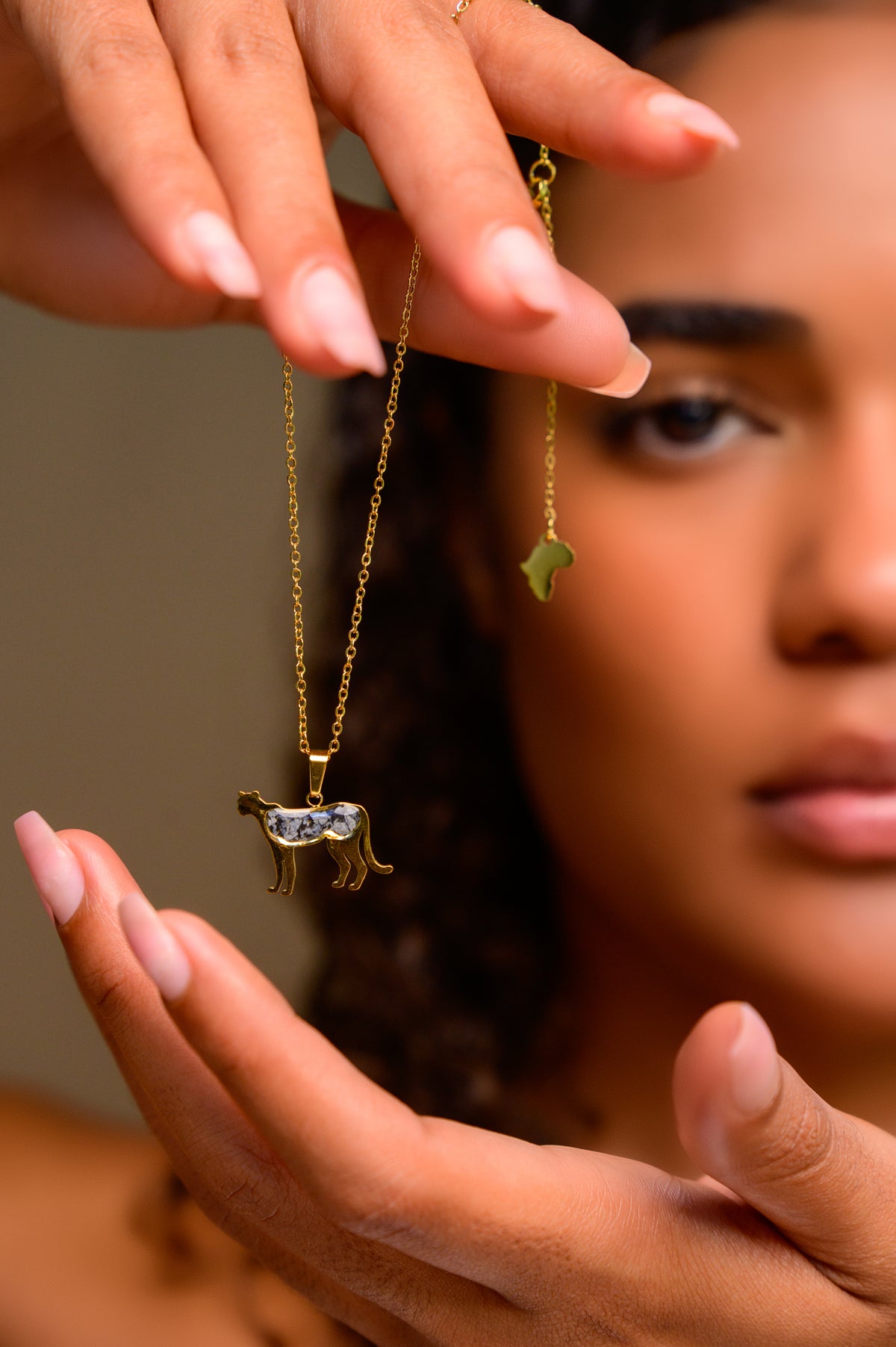 Close-up of a model's hand holding a necklace to show the adjustable extension chain and small Africa-shaped charm at the clasp end (charm pendant shown is for illustration of the extender mechanism only)