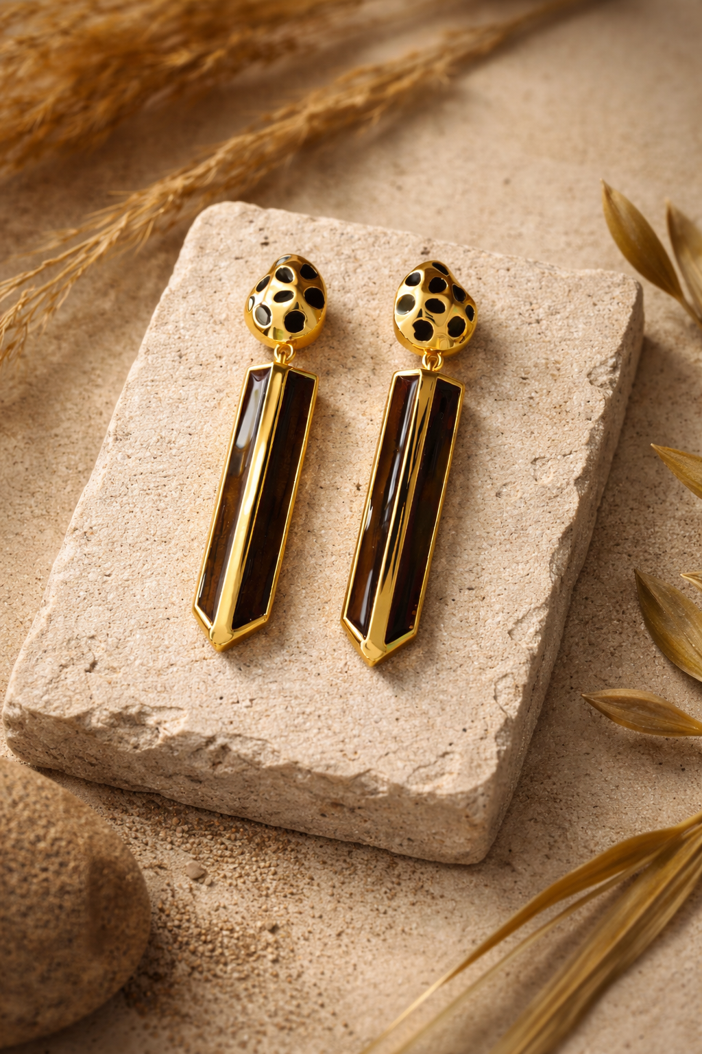 Gold-plated cheetah-print drop earrings with genuine wood inlay, styled on a stone slab with dried grasses