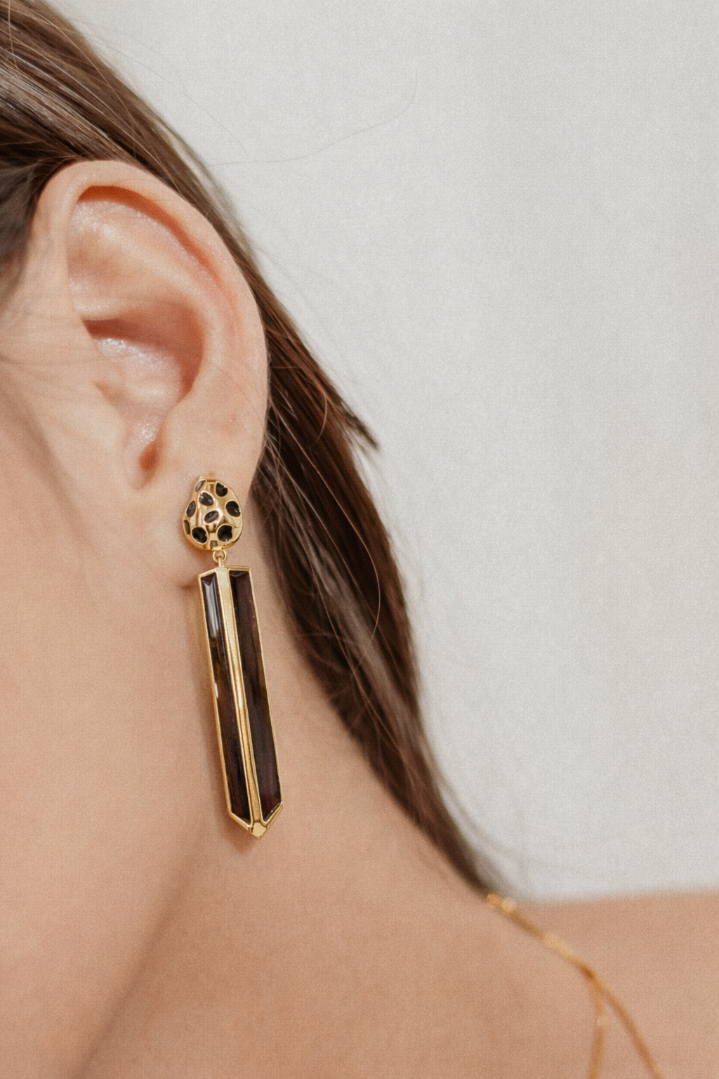 Close-up of a model's ear wearing gold-plated cheetah-print drop earrings with genuine wood inlay