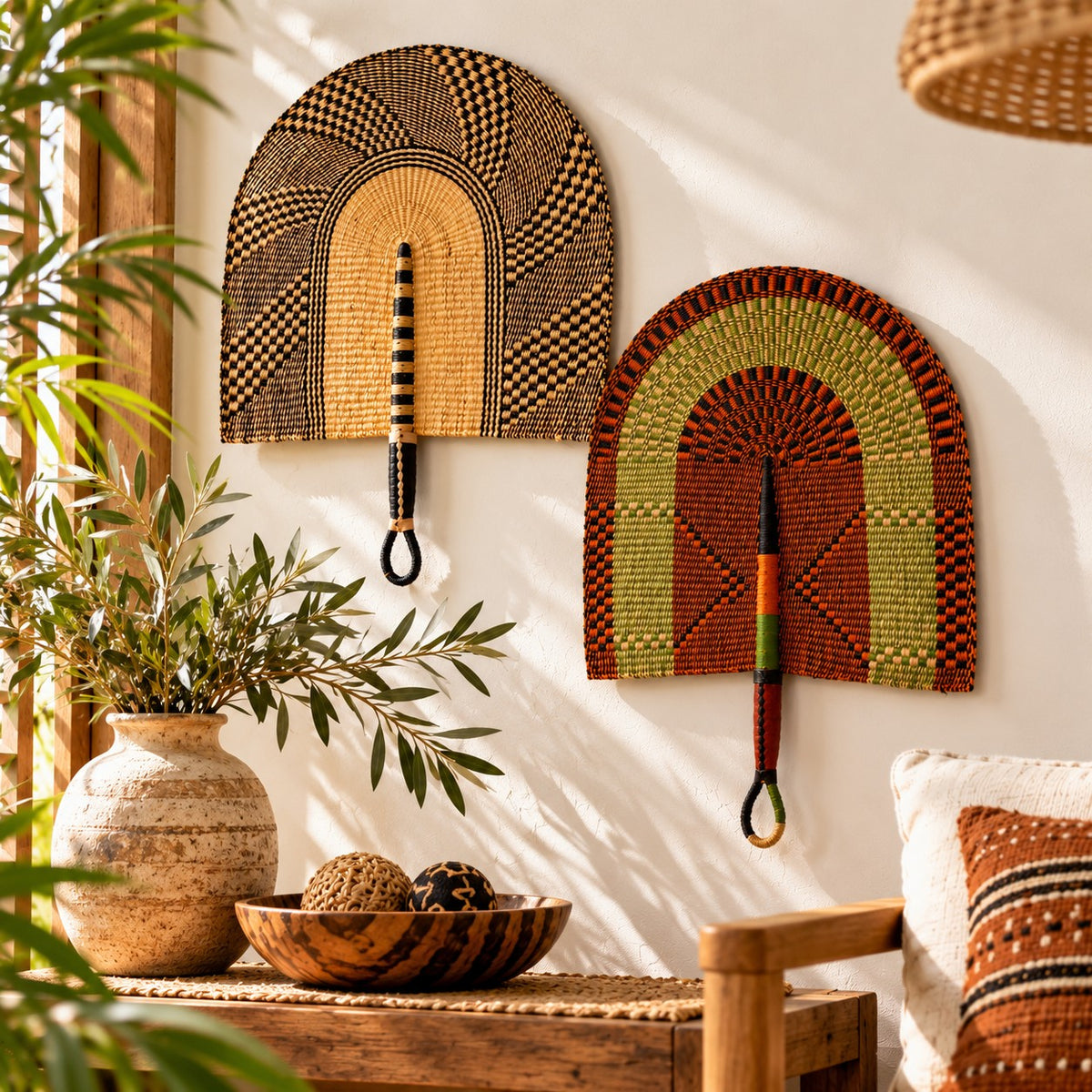 Two handwoven Bolga wall fans styled on a cream living room wall above a wooden side table with a vase and plant