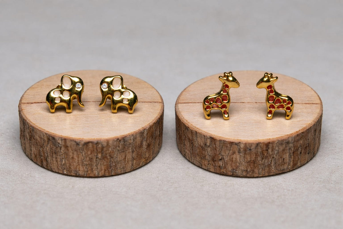 Little Wild gold-plated elephant stud earrings with mother-of-pearl spots and a cubic zirconia eye on a wooden slice, next to the matching Little Wild giraffe studs.
