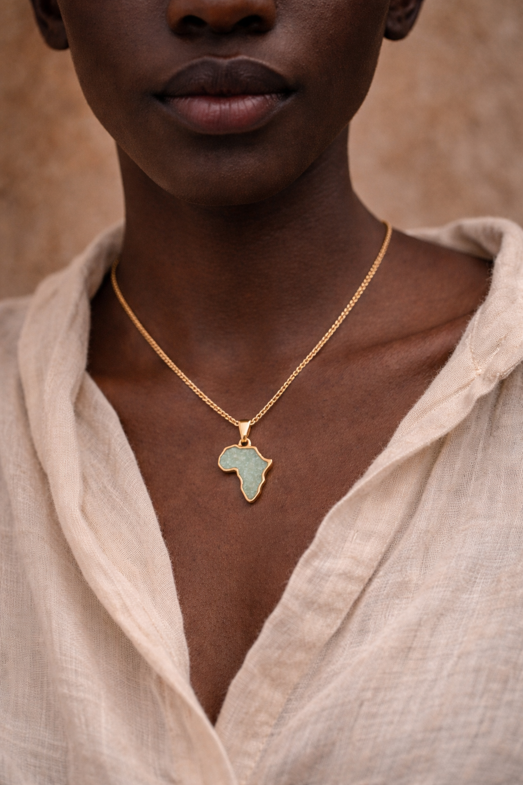 Close-up of a woman wearing a gold-plated Africa map necklace with a sea-green amazonite inlay, layered over a beige linen shirt.