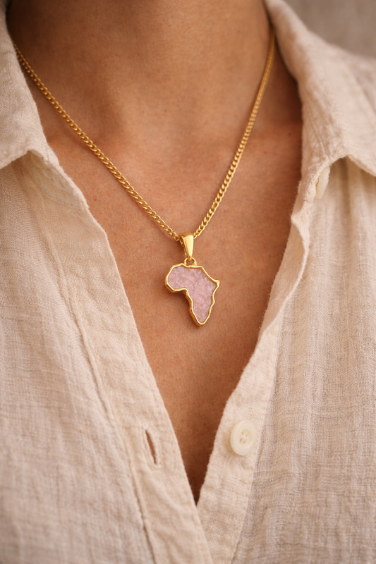 Close-up of a woman wearing a gold-plated Africa map necklace with a pink rose quartz inlay, layered over a cream linen shirt.