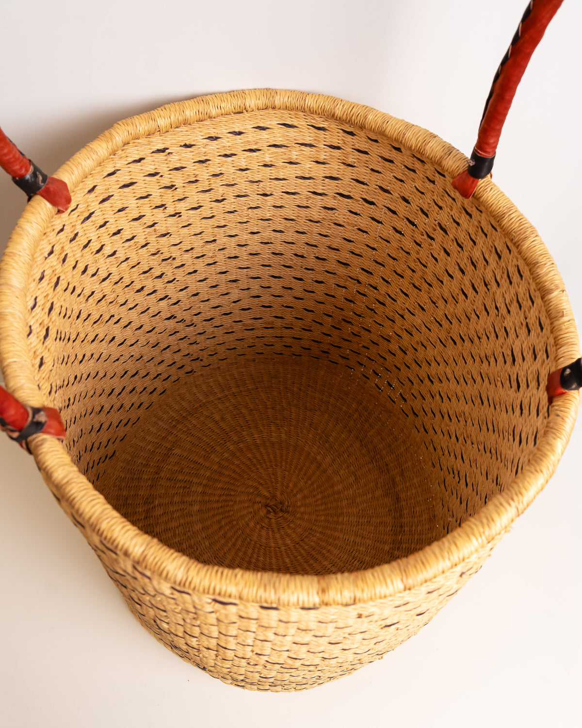 Top-down view into an empty brown and tan Bolga laundry basket, showing the handwoven spiral coil base in elephant grass, Ghana