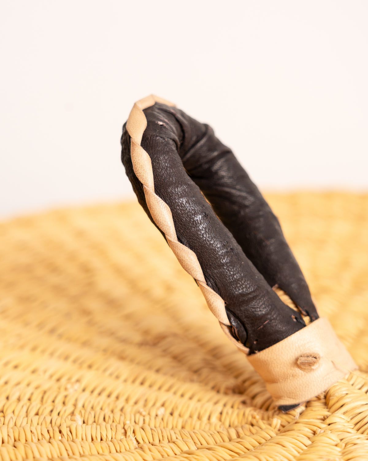 Close-up of the leather-wrapped handle on a natural tan Bolga laundry basket, two-tone braided leather on handwoven elephant grass, Ghana