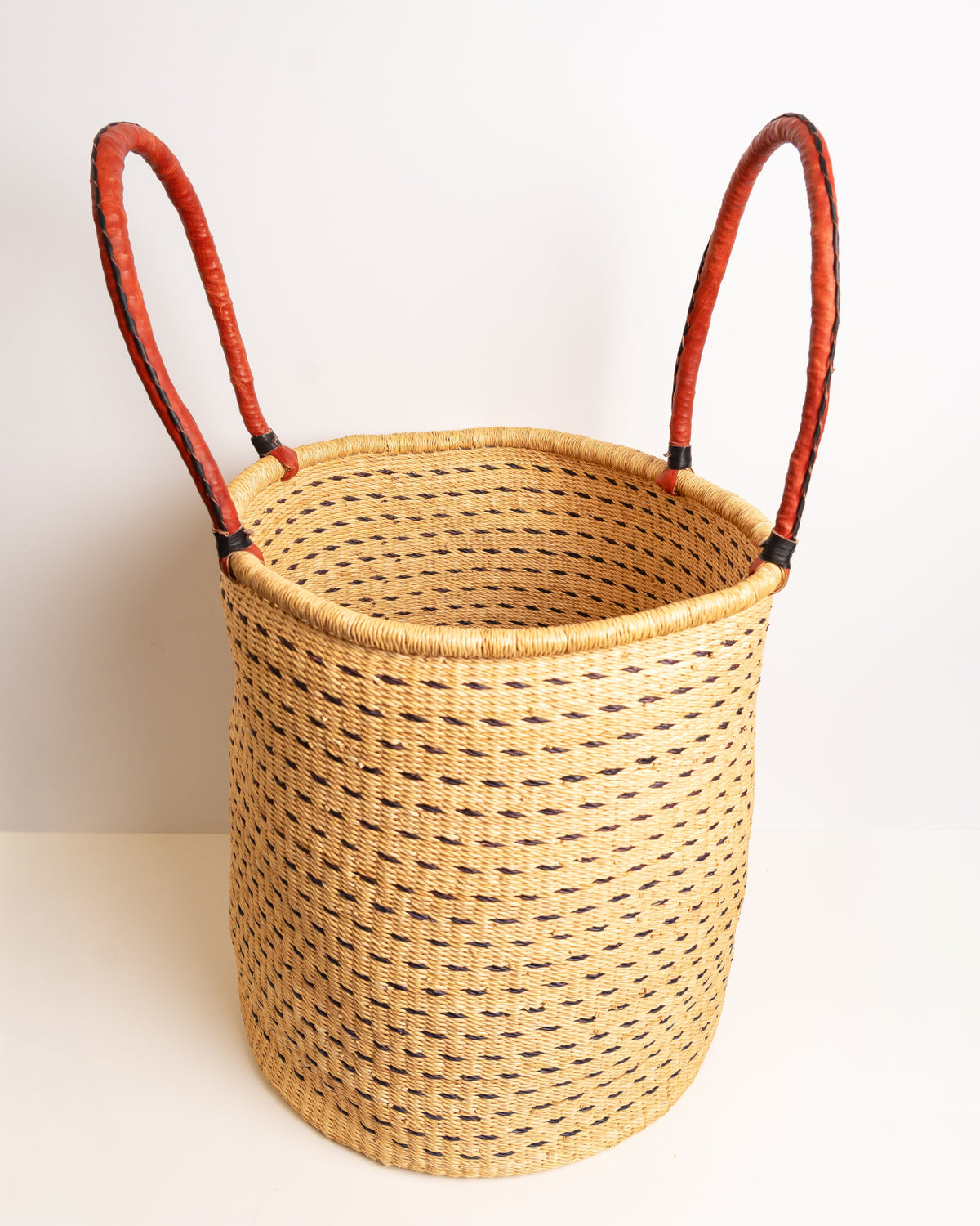 Angled view into an open brown and tan Bolga laundry basket, showing the hollow interior and leather loop handles, handwoven elephant grass, Ghana