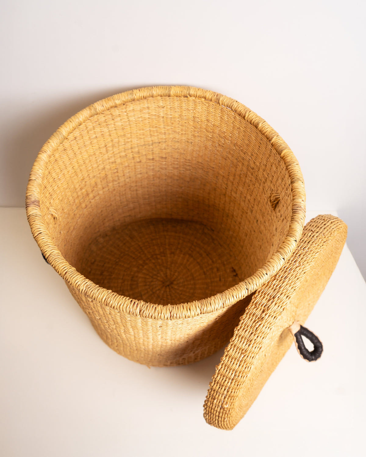 Top-down view into an empty natural tan Bolga laundry basket, showing the handwoven spiral coil base in elephant grass, Ghana