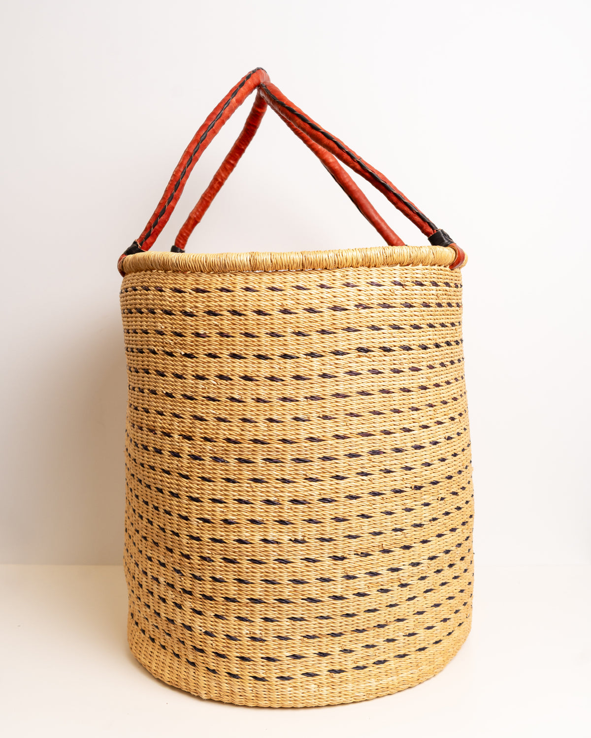 Brown and tan Bolga laundry basket with tall leather-wrapped loop handles, dark brown dash weave on natural tan elephant grass, Ghana