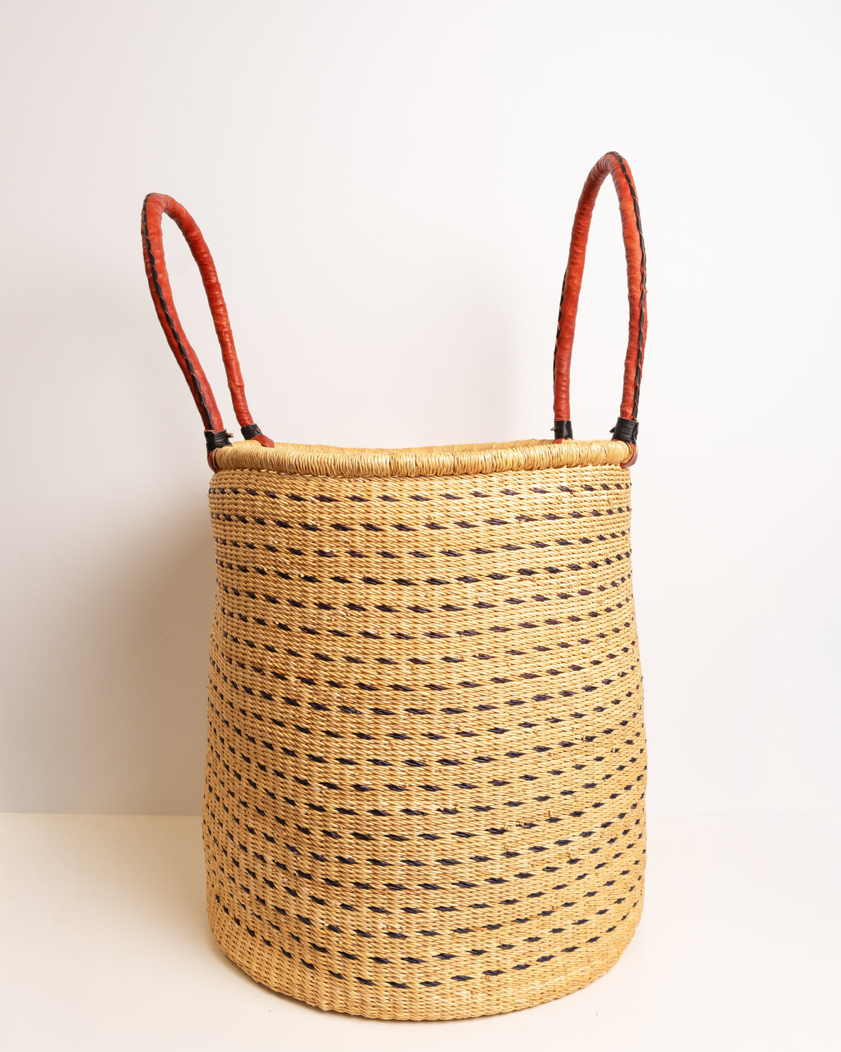Brown and tan Bolga laundry basket with open loop handles splayed outward, showing the open-top rim and dash weave pattern, handwoven elephant grass, Ghana